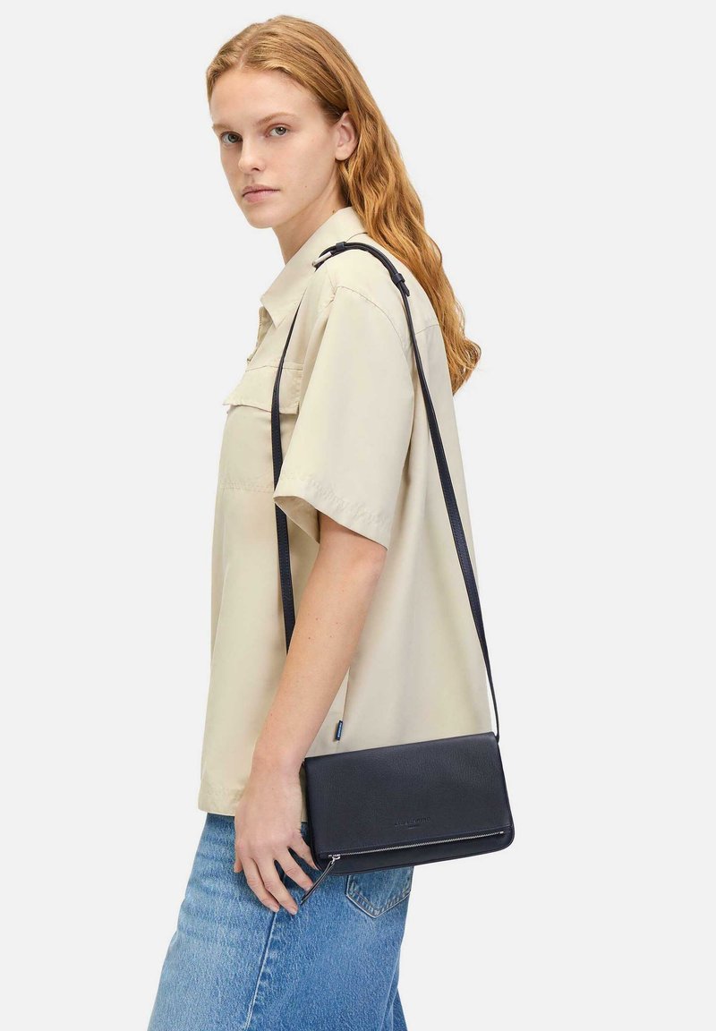 Czarna skórzana torba na ramię o gładkiej fakturze, prostokątnym kształcie i regulowanym pasku, z zamknięciem na zamek błyskawiczny oraz subtelnym brandingiem.