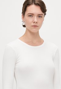 Camisola branca de manga longa em malha canelada com decote redondo. Textura suave e design justo, acentuando a forma do corpo.