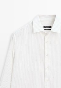 Chemise blanche à manches longues avec boutons, rayures fines grises verticales et col pointu, étiquette Massimo Dutti, fabriquée en Égypte.