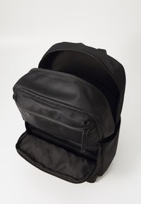 Černý batoh vyrobený z hladké tkaniny, s hlavní přihrádkou a přední kapsou na zip, obě s černými zipy a měkkým vnitřním podšívem.