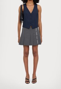 Marinblå väst med tre knappar, i kombination med en grå plisserad kjol med vertikala ränder och texten "LONG STORY VERY SHORT" i vitt.