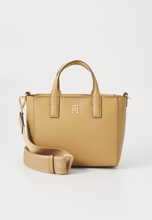 Lys håndveske laget av teksturert skinn med to håndtak og en avtagbar skulderreim. Har et gulllogo på fronten.