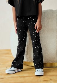 Mustad kõrgvööst püksid valge tähemustriga, kombineeritud hallide tossudega, millel on valge tallaosa ja mustad detailid.