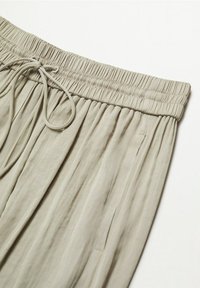 Pantalon beige clair à cordon de serrage avec taille élastique et poche latérale, fabriqué en tissu doux et fluide.