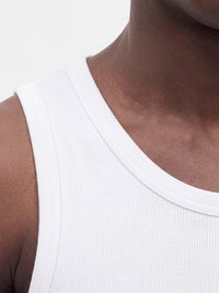 Close-up of a person’s shoulder and neck wearing a white ribbed tank top on a plain light background.