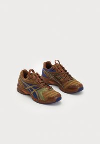 Bruna träning skor med meshnätpaneler, blå och gröna detaljer och texturerade sulor. Har snörning och en vadderad krage för komfort.