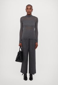 Graues, langärmeliges, eng anliegendes Oberteil und weite graue Hose. Strukturiertes Strickoberteil, glatte Stoffhose. Eine schwarze Handtasche und ankelschaftige Stiefel vervollständigen das Outfit.