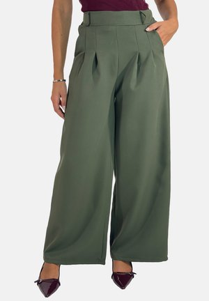 Pantaloni a gamba larga in tessuto verde oliva con pieghe davanti, vita alta e tasche laterali, abbinati a scarpe in vernice scura.