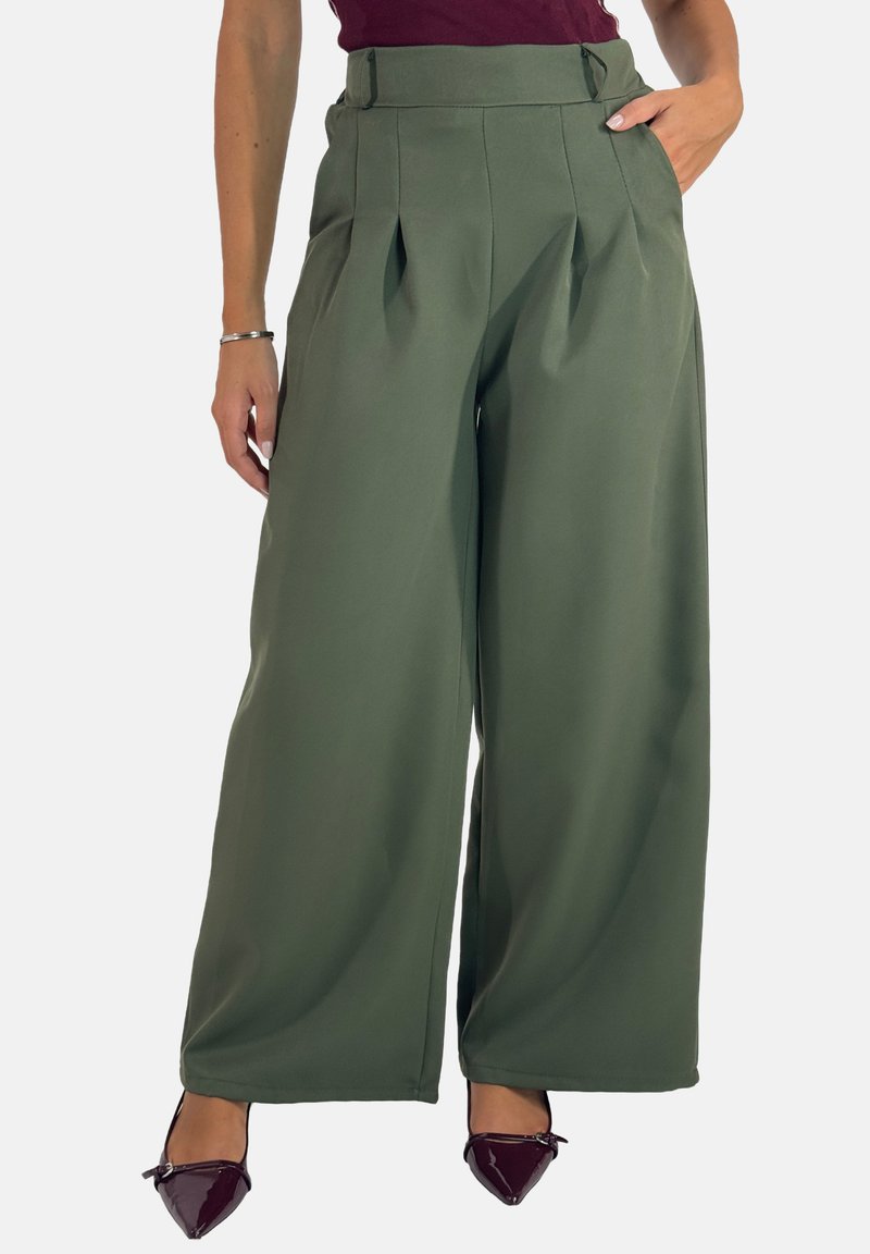 Olijfgroene wijde broek van stof met plooien aan de voorkant, hoge taille en zijzakken, gecombineerd met donkere gepatineerde schoenen.