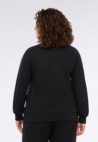 Felpa nera con una vestibilità comoda, caratterizzata da maniche raglan e un motivo testurizzato lungo le spalle. Tessuto morbido e polsini a coste.