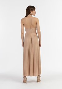 Dlouhé šaty bez zadního dílu z jemné metalické látky v odstínu růžového zlata. Mají plisovanou sukni, zúžený pas a design s halter krkem.