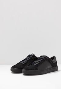 Mustat lenkkarit, joissa on yhdistelmä mokkaa ja nahkaa. Ominaisuuksiin kuuluu pyöreät kengännauhat, kumipohja ja huomaamaton brändäys sivulla.