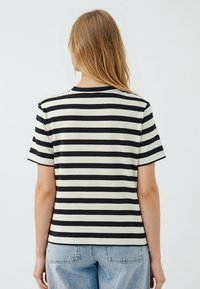 T-shirt a righe con un motivo nero e crema, maniche corte, collo rotondo, realizzata in materiale morbido. Presenta una vestibilità rilassata.