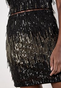 Schwarzes Kleid mit vertikalen Fransen und metallischen Pailletten. Hat eine taillierte Silhouette mit unterschiedlichen Texturen und glänzenden Akzenten.