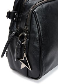 Bolso de cuero negro con acabado texturizado, con cierre de cremallera, correa ajustable y un charm en forma de estrella plateada adjunto.