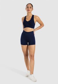 Set van sportbeha en high-waist shorts in marineblauw, gemaakt van rekbare stof met een gladde textuur, voorzien van uitsnijdetails en logo-accenten.