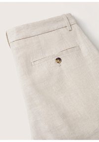 Jasnobeżowe lniane spodnie z jedną tylną kieszenią, zamykane na okrągły guzik. Gładka faktura z subtelnym, naturalnym splotem.