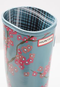 Cubeta de basura Hunter, azul con diseño de flores de cerezo. Acabado suave, el interior presenta un patrón a cuadros en negro y azul. Bisel superior inclinado.