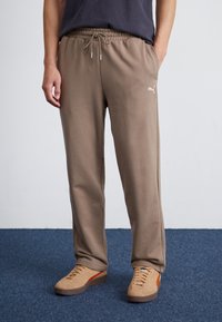 Braune Jogginghosen mit einem elastischen Bund und Schnürdetails; kombiniert mit tanfarbenen Sneakers mit einem orangefarbenen Streifen.