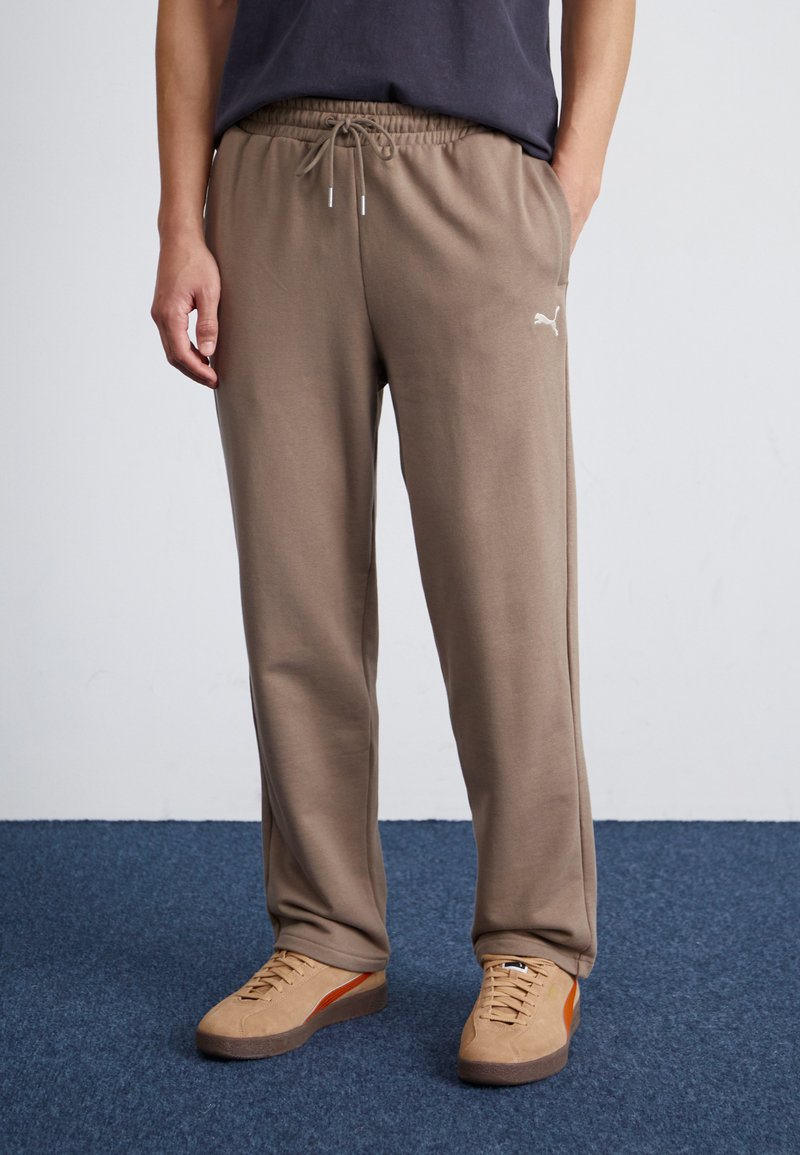 Braune Jogginghosen mit einem elastischen Bund und Schnürdetails; kombiniert mit tanfarbenen Sneakers mit einem orangefarbenen Streifen.