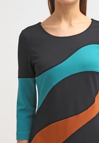 Robe noire avec des motifs ondulés teal et marron, dotée d'un encolure ronde et de manches trois-quarts, fabriquée en tissu lisse et extensible.