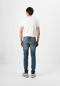 Kék, egyenes szabású farmernadrág, klasszikus zsebdarabbal, hátul, a derék résznél barna bőr címkével.