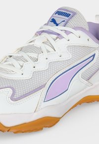 Άσπρο και λεβάντας αθλητικό παπούτσι Puma με ανώτερο μέρος από δίχτυ, λευκά κορδόνια, μοβ λογότυπο και πορτοκαλί λαστιχένια σόλα.