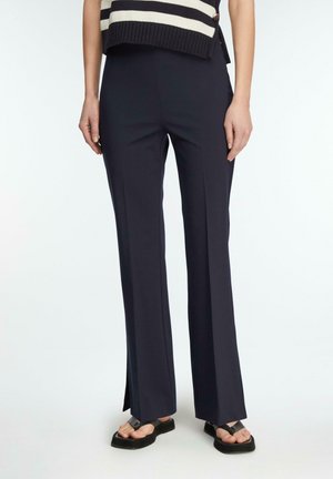 Kobieta ubrana w granatowe spodnie o szerokich nogawkach z bocznymi rozcięciami, czarne sandały na platformie oraz czarno-biały, bezrękawnik w paski.