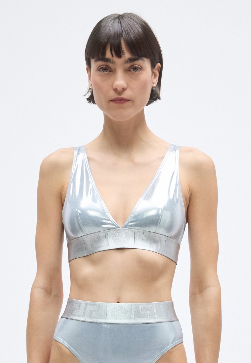 Ezüst fényes melltartó mély V-nyakkal és széles derékpánttal, amely geometrikus mintával díszített. A szetthez magasderekú, hozzáillő alsó tartozik.