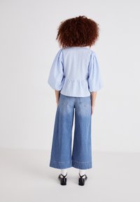Blusa a quadretti blu e bianchi con maniche a sbuffo, vita cinte e jeans in denim blu chiaro a gamba larga con effetto sbiadito e orlo sfrangiato.
