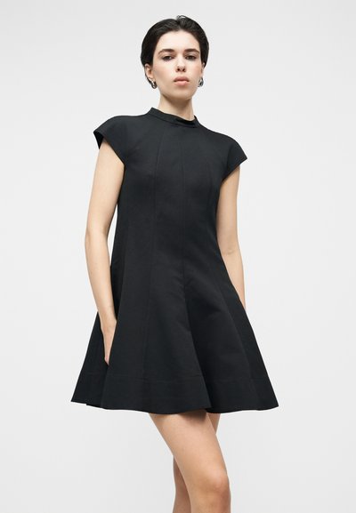 Juoda trumpa suknelė su aukšta apykakle ir trumpomis rankovėmis. Į liemenį siaurėjanti linija, su šoninėmis kišenėmis ir struktūruota medžiaga. Paprastas, švarus dizainas.