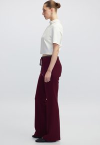 Witte crop top met hoge kraag, gecombineerd met bordeaux brede broek met een drawstring taille. Zwarte gestructureerde schoenen maken de look af.