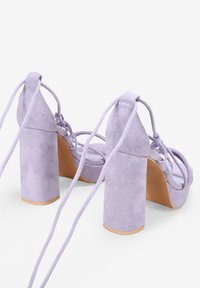 Sandalias de tacón alto de ante lila con puntera cuadrada, gruesos tacones en bloque y correas de lazada. Textura suave y suela de goma sólida.