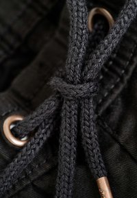 Primer plano de cordones trenzados negros atados en un nudo a través de ojales de metal bronce en tela negra.