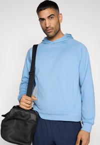 Sweat à capuche bleu clair avec une poche avant et une capuche à cordon, associé à un pantalon bleu marine foncé. Sac bandoulière noir avec une surface texturée.