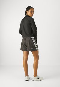 Jaqueta preta cropped com mangas longas, combinada com calções cinzentos com riscas brancas. Os sapatos são brancos com detalhes pretos.