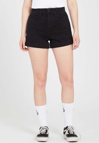 Shorts en denim noir avec une taille haute, des revers roulés et des poches avant. Associés à des chaussettes blanches montantes et des baskets noires. Texture lisse.