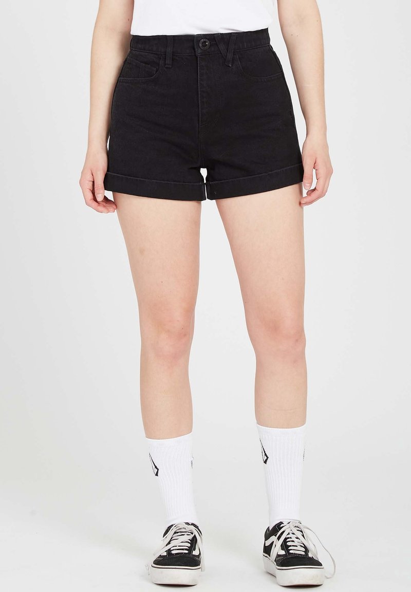 Shorts en denim noir avec une taille haute, des revers roulés et des poches avant. Associés à des chaussettes blanches montantes et des baskets noires. Texture lisse.