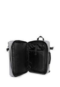 Zaino in tessuto grigio con interno nero, dotato di una chiusura con zip singola, tasche interne e una maniglia per il trasporto superiore.