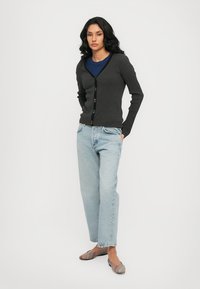 Cardigan a righe grigio scuro con scollatura a V, caratterizzato da una fila di bottoni multicolori. Abbinato a jeans a gamba dritta blu chiaro e ballerine con fantasia.