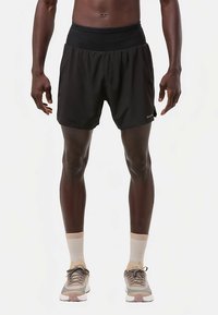 Mustad sportlühikesed püksid elastse vöökohaga, valmistatud kergest kangast, kombineeritud beežide ja hallide tossudega ning pahkluu pikkuste sokkidega.