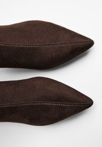 Pantofi maro închis din suede cu vârf ascuțit, prezentați din perspectiva superioră pe un fundal alb, evidențiind detaliile cusăturii de-a lungul centrului.