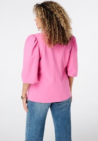 Roze blouse met pofmouwen van textiel, aansluitend bij het lijfje, met een achterkantnaaddetail, gecombineerd met lichtblauwe wijde jeans.