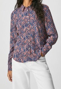 Blommig långärmad skjorta i marinblått med rosa och vita blommor, knäppning fram, krage och avslappnad passform. Bärs tillsammans med vita byxor.