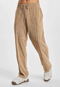 Beige fleece drawstring pants worn with white and brown Nike sneakers on a white background, cropped at the waist.