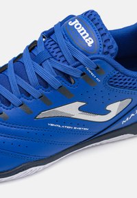 Blue sports shoe with a mesh upper, reinforced toe, silver logo, and ventilation accents; features flat laces and textured sole.