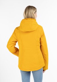 Chaqueta impermeable amarilla con capucha, que presenta una textura suave y un corte entallado, extendiéndose hasta las caderas. La vista trasera muestra detalles de costura en contraste.