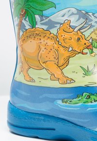 Blauwe rubberen laars met een dinosaurusscene, inclusief een oranje dinosaurus die vegetation eet, met palmbomen en bergen op de achtergrond.
