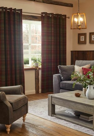 Gemütliches Wohnzimmer mit karierten Vorhängen, grauem Sessel, grauem Sofa mit Kissen, hölzernem Couchtisch, Zimmerpflanzen und einer Hängeleuchte.
