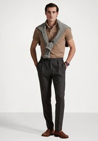 Μπεζ πόλο πουκάμισο, γκρι πλεκτό πουλόβερ περασμένο πάνω από τους ώμους, ραμμένο σκούρο παντελόνι και καφέ δερμάτινα παπούτσια. Απλό ρολόι στον καρπό.